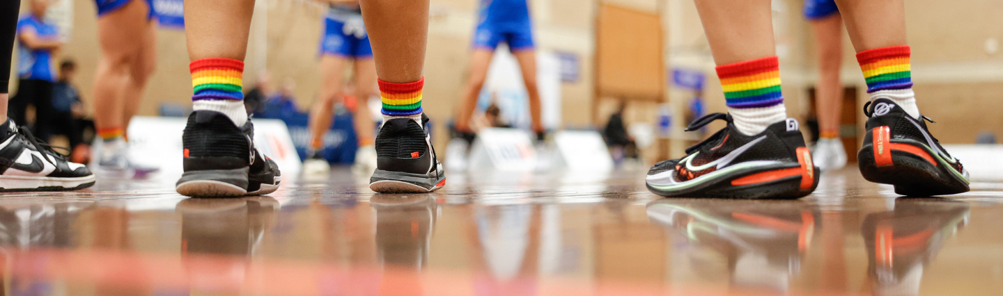 Legs of two athletes wearing rainbow socks on a reflective basketball court