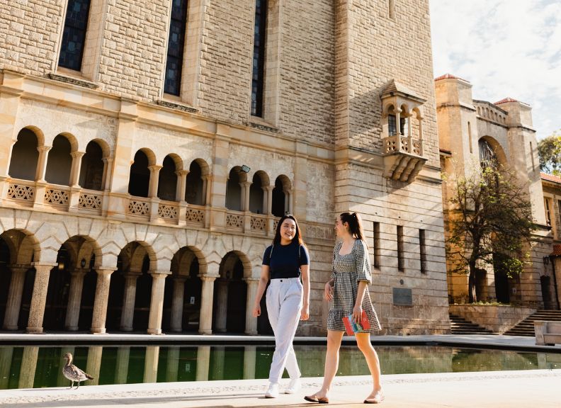 Students walking by Reflection Pond with Winthrop Hall in background.