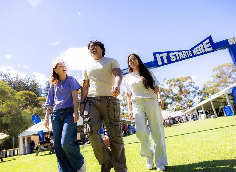 Image of 3 students walking away from a sign that reads 'It Starts Here' at Open Day
