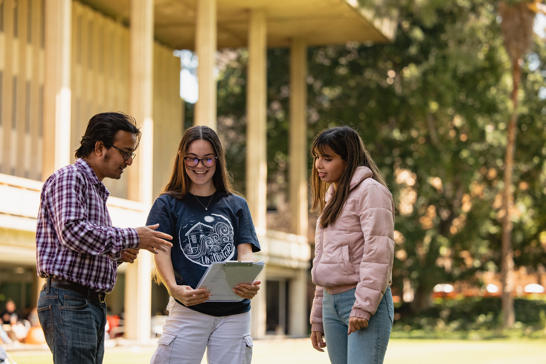 Student mentors providing support on Great Court near Reid Library. The student mentor has a clipboard they are showing the other two students.
