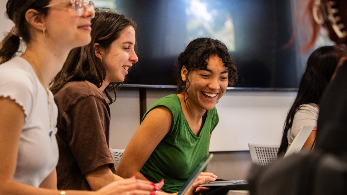 A close view of a group of females smiling in the classroom with laptops