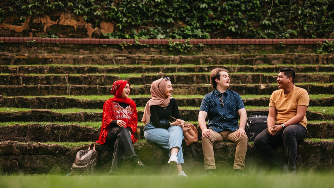 Four students sitting in Sunken Garden and laughing