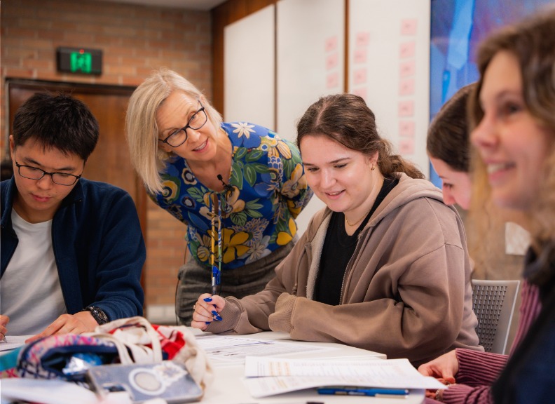 Academic assisting and talking with four students in a classroom