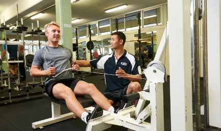 A sports science student using a piece of exercise equipment in the gymnasium and being guided by an instructor