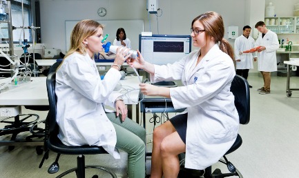 Two students testing their breath, using machine, in lab coats, in laboratory