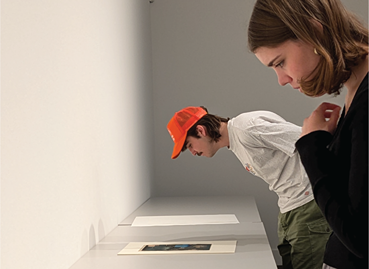 A mid shot of a female student with a male student further in the background, looking at an art display.