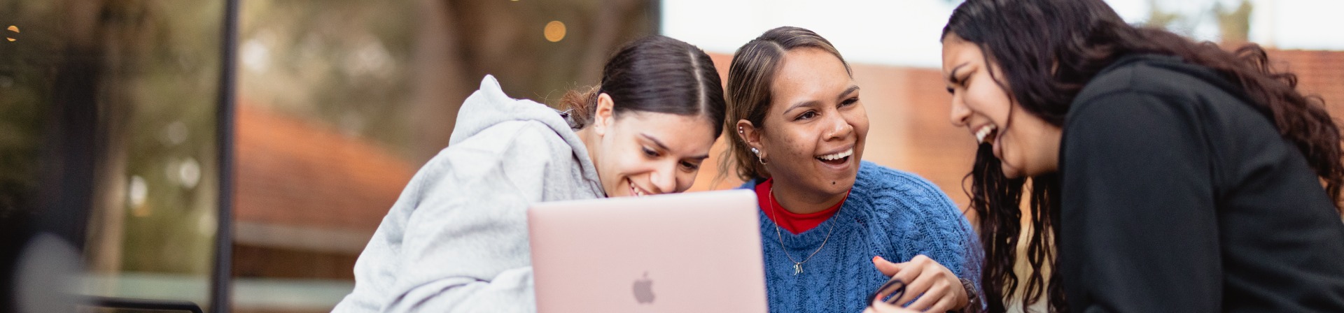 Three students sitting in front of laptop laughing